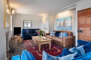 A living room with a blue sofa, a brown leather sofa, a wooden coffee table, a TV, a painting, and a wooden door.