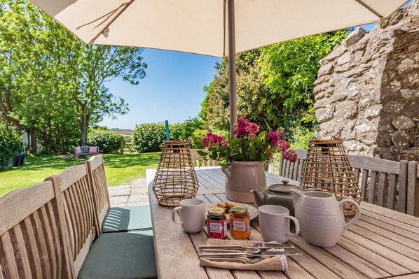 An outdoor patio with a table set for dining, surrounded by greenery and stone walls.