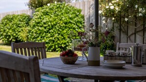 Een houten tafel met een schaal aardbeien, een vaas bloemen en een glas water.