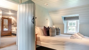 Een slaapkamer met een bed, kussens, een raam en een deur naar een andere kamer.