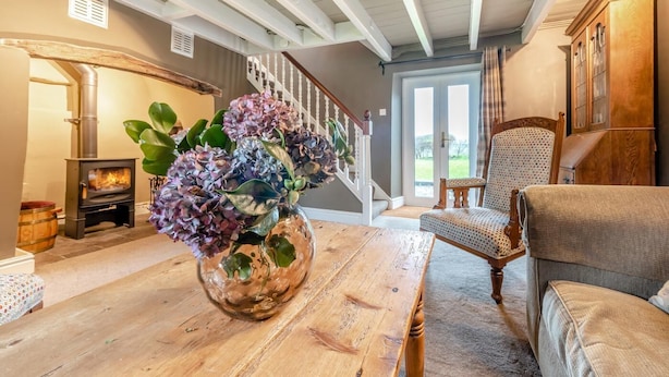 Een woonkamer met een houten tafel, een bloemenvaas, een bank, een stoel, een open haard en een trap.
