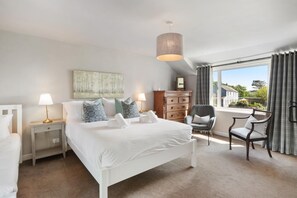A bedroom with a bed, two bedside tables, a dresser, a chair, a window with curtains, and a hanging light fixture.