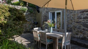 Un patio al aire libre con una mesa y sillas de madera, rodeado de muros de piedra y follaje.