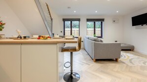 A modern kitchen with a wooden countertop, a bar stool, and a dining area with a sofa and a TV mounted on the wall. - 2 Bed in Padstow (oc-t30497) (Padstow)