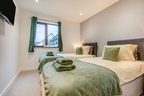 A hotel room with two beds, green curtains, a window with a view, and a flat-screen TV mounted on the wall. - 2 Bed in Padstow (oc-t30497) (Padstow)