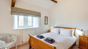A bedroom with a wooden bed, a window with a patterned valance, a wicker chair, and a bedside table with a lamp and a mug. - 4 Bed in Mallerstang (oc-s22487) (Mallerstang)