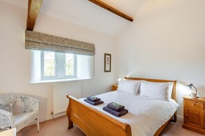 A bedroom with a wooden bed, a window with a patterned valance, a wicker chair, and a bedside table with a lamp and a mug. - 4 Bed in Mallerstang (oc-s22487) (Mallerstang)