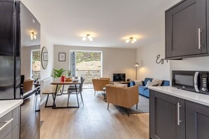 Una cucina moderna con pensili scuri, un'area pranzo con tavolo e sedie, un divano e una televisione.