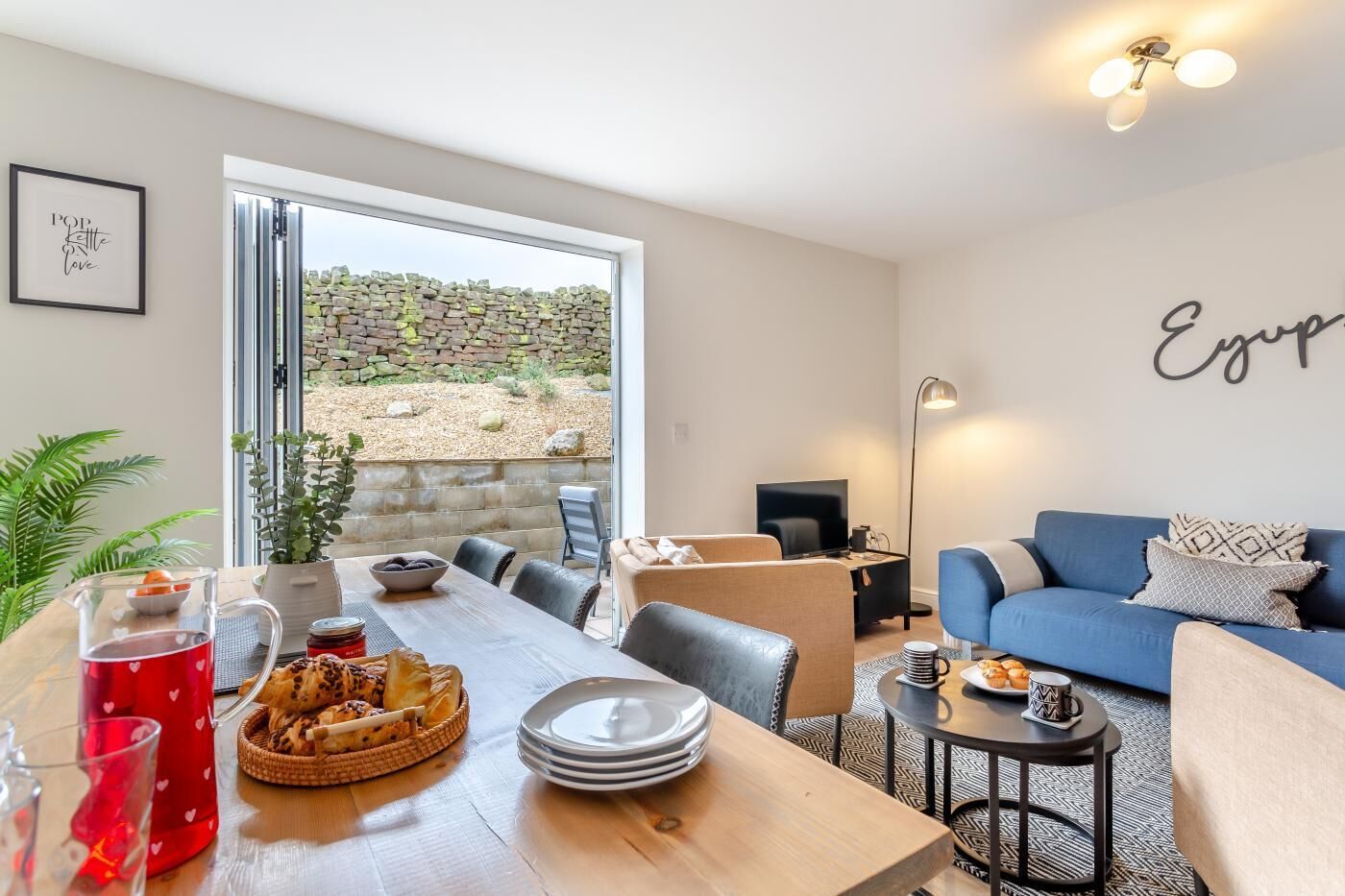 Un salon moderne comprenant un coin repas, un canapé bleu et un mur en pierre.