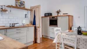 A compact kitchen with white cabinets, a wooden countertop, a microwave, and a dining area with a table and chairs. - 3 Bed in Brighstone (oc-r30510) (Brighstone)