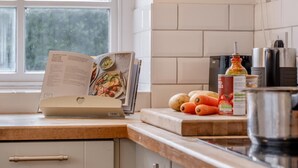 A kitchen with a cookbook open on the counter, a pot, and some vegetables. - 3 Bed in Brighstone (oc-r30510) (Brighstone)