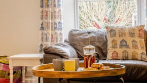 Uma sala de estar acolhedora com um sofá de couro, uma mesa de centro com uma bandeja de itens de café da manhã e uma janela com cortinas.