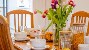 Mesa de pequeno-almoço posta para duas pessoas, com tigelas, copos, croissants e um vaso de tulipas.