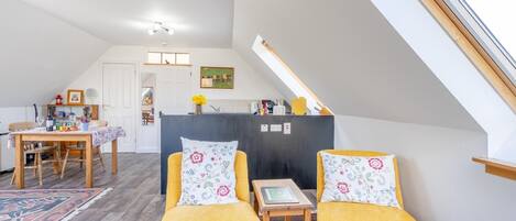 Et loft-studie med spiseplads, et lille bord med stole og udsigt til himlen gennem en ovenlys.