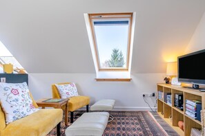 A cozy room with a sloped ceiling, a small window, a sofa, a chair, a TV, and a bookshelf. - 1 Bed in Methven (oc-v30533) (Methven)