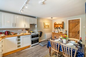Une cuisine compacte avec des meubles blancs, un plan de travail en bois et un coin repas avec une table dressée pour deux personnes.