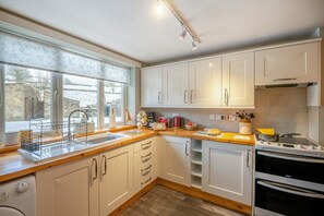 A modern kitchen with white cabinets, a wooden countertop, a built-in oven, and a window with a view of a stone building outside.