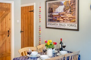 Un coin repas avec une table dressée pour quatre personnes, un tableau encadré représentant les chutes d’Aysgarth et une guirlande décorative de boules colorées.