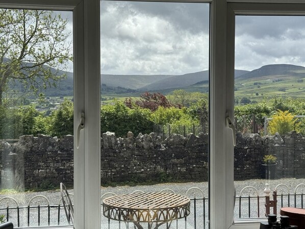 A room with a large window offering a view of a stone wall, a wooden table, and a chair.