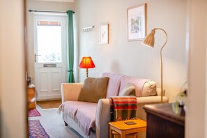 Un salon confortable avec un canapé, une lampe, une petite table et une vue sur l’extérieur.
