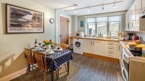 A compact kitchen with a dining area, a washing machine, and a large window. - 2 Bed in Hawes (oc-b30521) (High Abbotside)