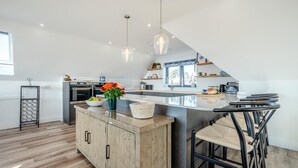 A modern kitchen with a central island, pendant lights, and a dining area with bar stools. - 4 Bed in Porthleven (oc-ch30536) (Porthleven)