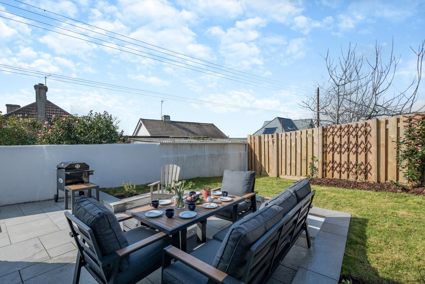 Une terrasse extérieure avec une table dressée pour quatre personnes, entourée de chaises et d’un banc.