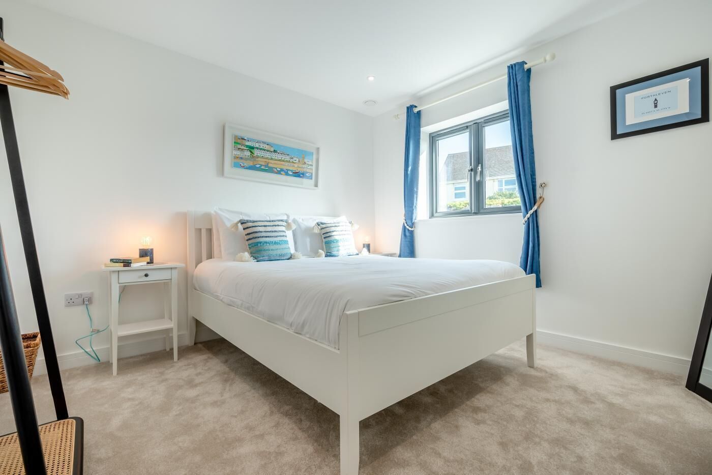 Une chambre à coucher avec un lit blanc, des rideaux bleus, une table de chevet, une lampe et un tableau encadré au mur.