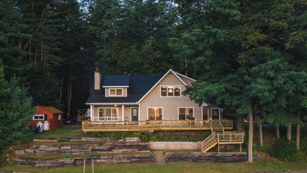 A two-story house with a deck, a staircase, and a dock extending into a body of water. - Waterfront Cabin with expansive deck near Saratoga & Lake George (Corinth)