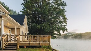 A house with a wooden deck, a porch, and a view of a lake with mist over the water. - Waterfront Cabin with expansive deck near Saratoga & Lake George (Corinth)