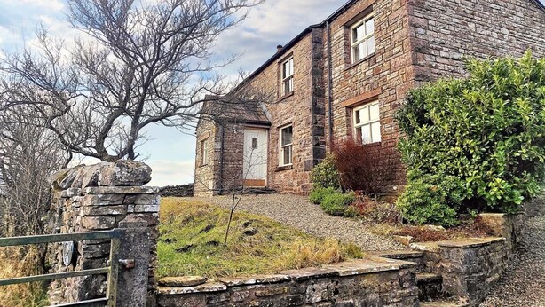 A stone building with a traditional design, featuring a central door and windows, surrounded by a gravel path and greenery. - 3 Bed in Garsdale (oc-l30314) (High Abbotside)