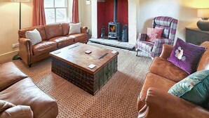 A cozy living room with a fireplace, leather sofas, and a plaid armchair. - 3 Bed in Garsdale (oc-l30314) (High Abbotside)