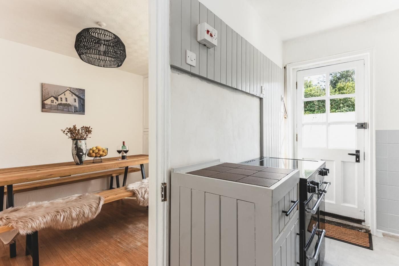 Une cuisine moderne dotée d’une cuisinière intégrée, d’un banc agrémenté d’un plaid en fourrure et d’une table à manger ornée d’un vase et de verres à vin.
