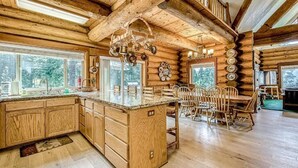 A wooden cabin interior with a kitchen island, dining table, and chairs. - Regatta Chalet – Premium Lakeshore Retreat (Lakeshore)