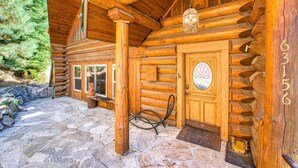 A log cabin with a stone-paved entrance, a wooden door with a circular emblem, and a stone bench outside. - Regatta Chalet – Premium Lakeshore Retreat (Lakeshore)