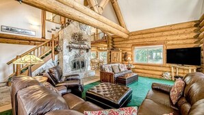 A log cabin interior with a stone fireplace, leather sofas, and a television. - Regatta Chalet – Premium Lakeshore Retreat (Lakeshore)