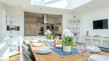 A modern dining area with a wooden table set for a meal, a kitchen in the background, and a skylight above.