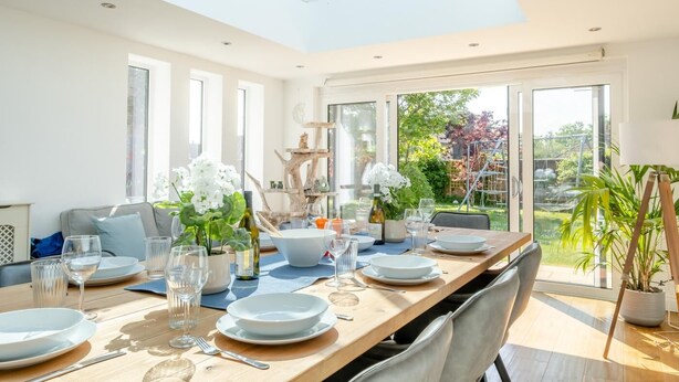 Comedor con una larga mesa dispuesta para seis personas, ventanas amplias y vista al jardín.