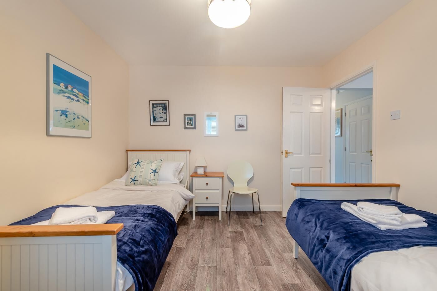 A bedroom with two beds, a chair, a nightstand, and a door.