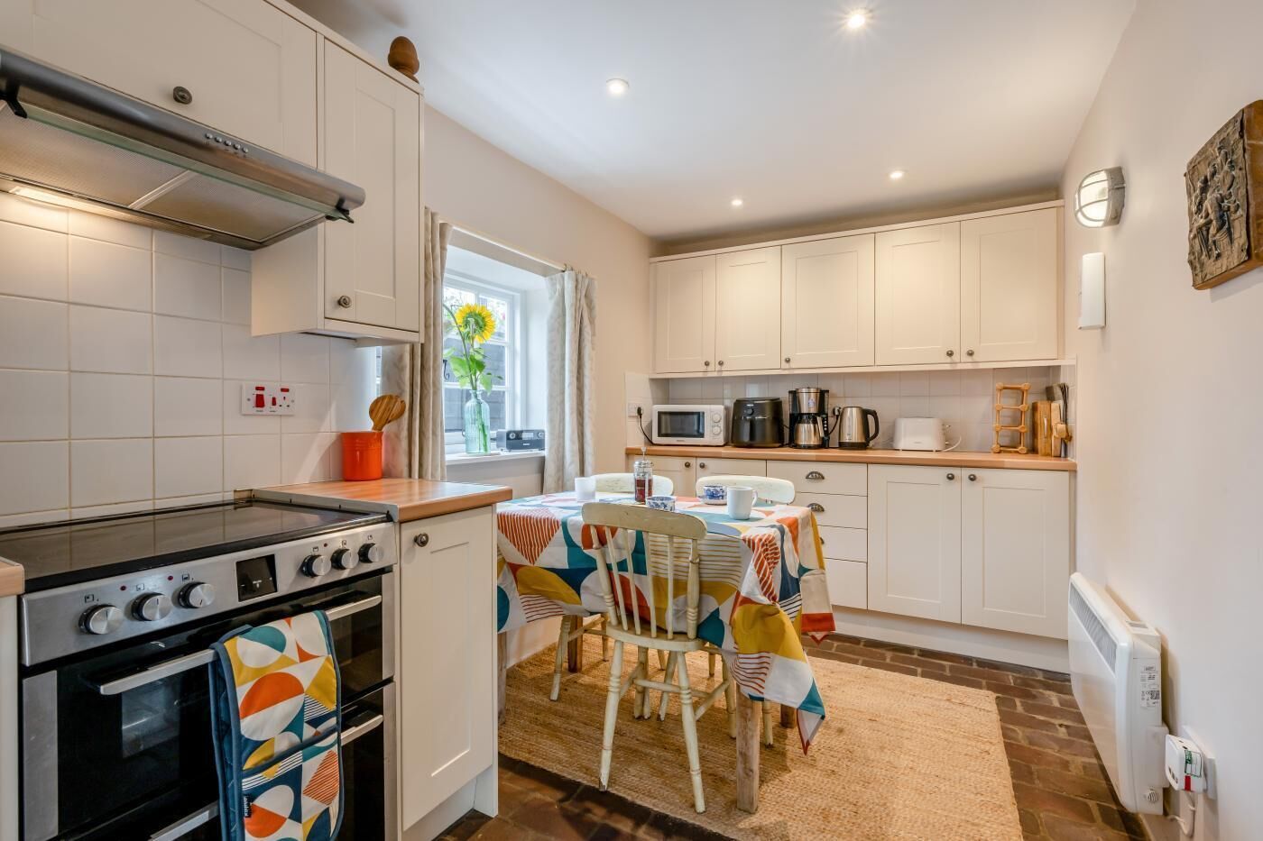 A compact kitchen with white cabinets, a stove, and a dining table set for two.