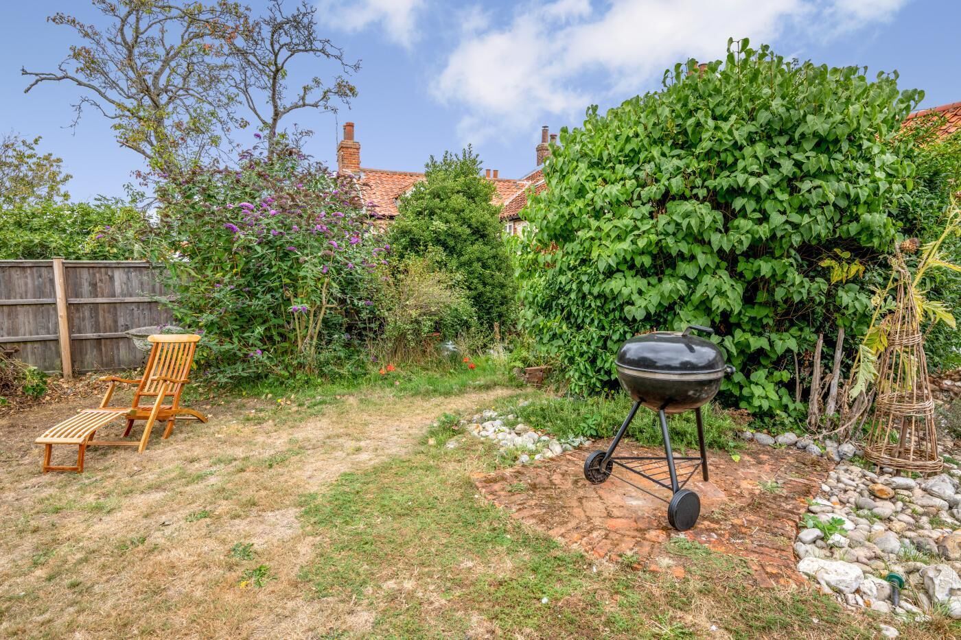 A backyard with a wooden chair, a barbecue grill, and a garden with various plants and a fence.