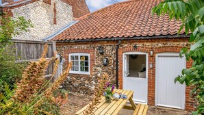 Een landelijke woning met een gevel van steen en baksteen, een pannendak en een houten tafel met terrasmeubels.