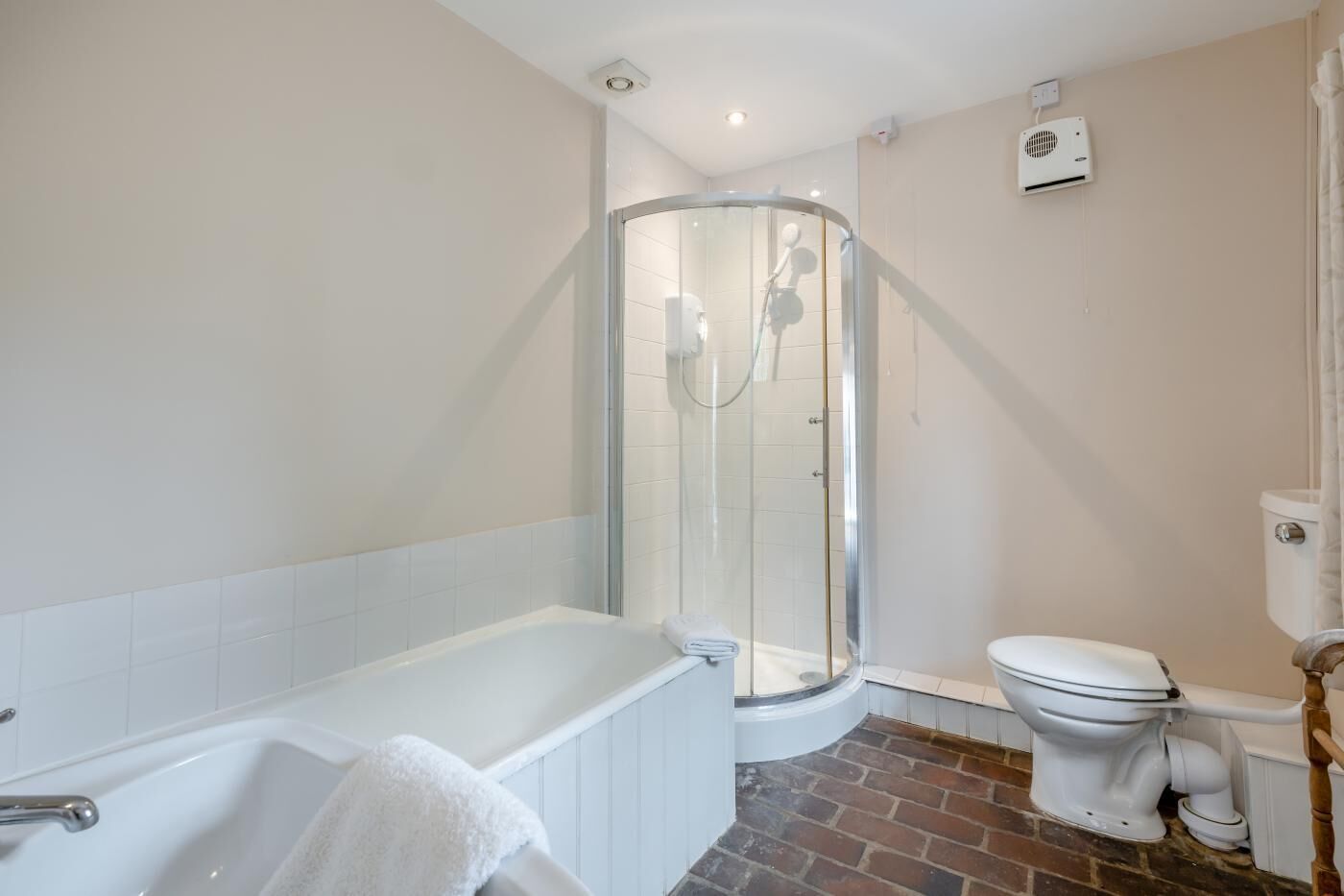 A bathroom with a glass-enclosed shower, a white bathtub, and a toilet.