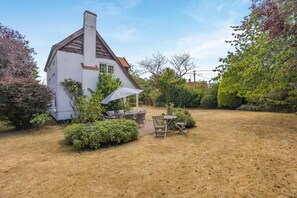 A white house with a pitched roof and a chimney, surrounded by a garden with a patio table and chairs. - 3 Bed in Walberswick (oc-e30479) (Walberswick)