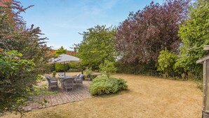 Eine Terrasse mit Tisch und Stühlen, umgeben von einem Garten mit verschiedenen Pflanzen und Bäumen.
