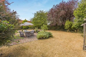 A patio area with a table and chairs, surrounded by a garden with various plants and trees. - 3 Bed in Walberswick (oc-e30479) (Walberswick)