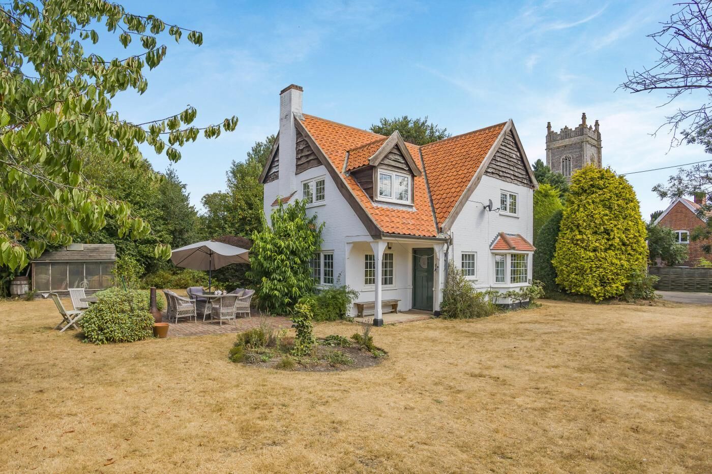 A two-story house with a red-tiled roof, a chimney, and a large garden with a patio area.