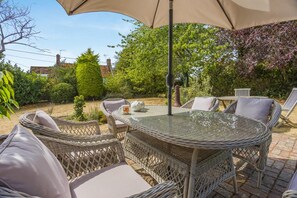 An outdoor patio with wicker furniture, a glass table, and a large umbrella providing shade.