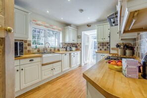 A kitchen with white cabinetry, a wooden countertop, a microwave, a sink, and a window with a view of the outdoors.