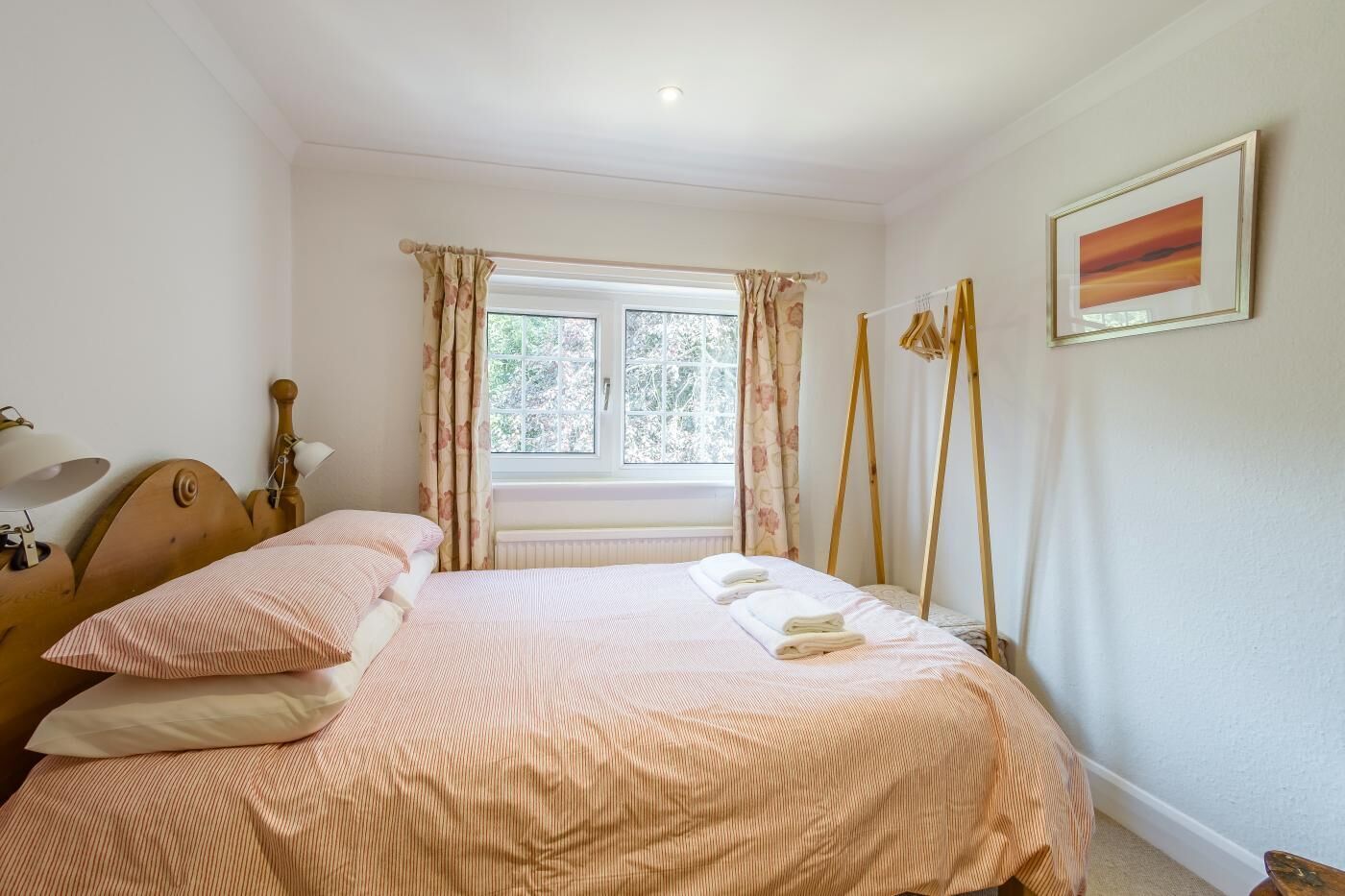 A bedroom with a bed, a window, a bedside table, and a wall-mounted picture.